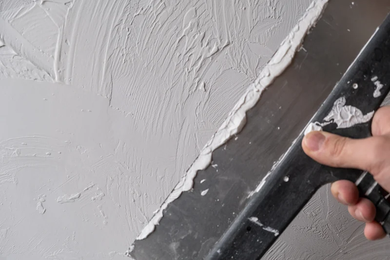 Trowel working wet compound across a textured wall