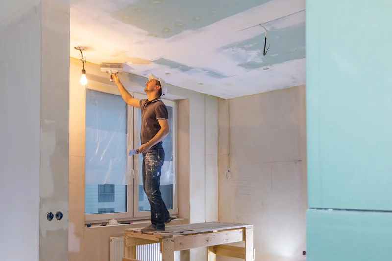 Worker on a platform finishing a ceiling beside a window