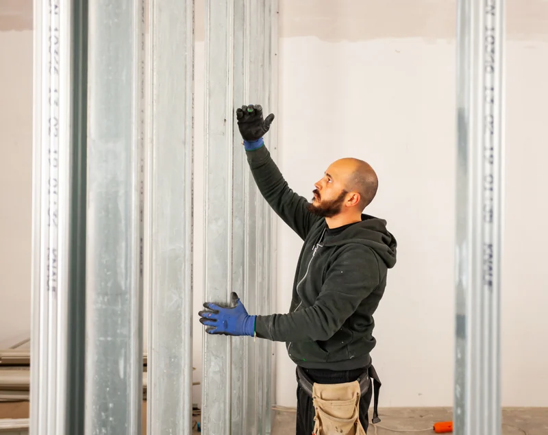 Worker standing between light-gauge steel studs on a new partition