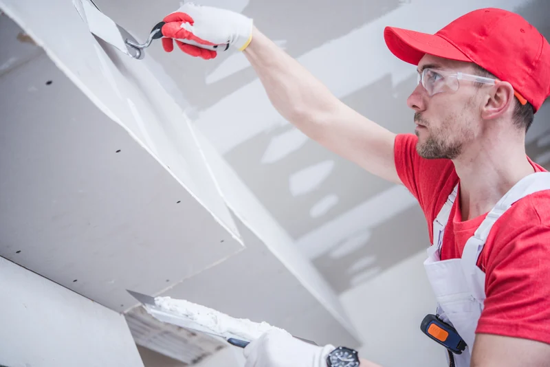 Worker cutting a drywall sheet overhead at a ceiling