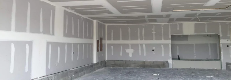 A garage-sized room boarded and taped throughout, with a bare concrete floor and one unfinished patch of board