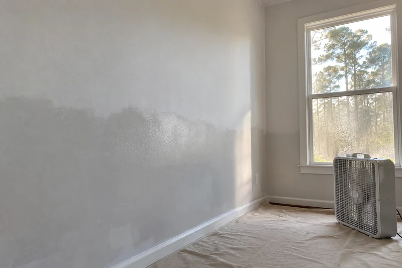 Primer still damp across the lower wall with a box fan moving air over it